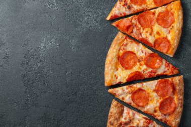 Dilimleri lezzetli taze pizza sosis sucuk ve peynir ile karanlık bir arka plan üzerinde kesmek. Üstten görünüm metin için kopya yer ile. Pizza siyah beton masada. düz lay.