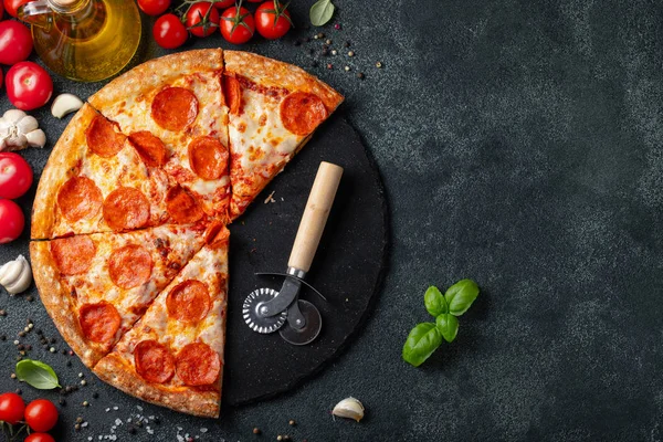 Tasty pepperoni pizza and cooking ingredients tomatoes basil on black concrete background. Top view of hot pepperoni pizza. With copy space for text. Flat lay.