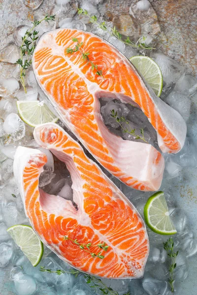 Two raw fresh salmon or trout steaks on ice, rich in omega-3 oil, with lime, thyme and olive oil on a blue rusty background. Healthy and dietary food. Top view. Flat lay.