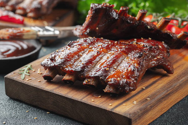 Closeup of pork ribs grilled with BBQ sauce and caramelized in honey. Tasty snack to beer on a wooden Board for filing on dark concrete background.