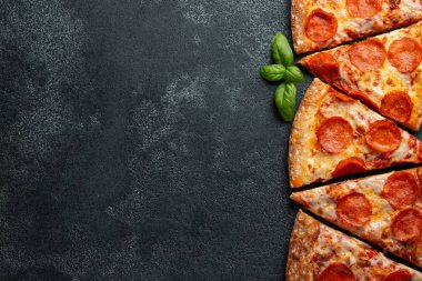 Dilimleri lezzetli taze pizza sosis sucuk ve peynir ile karanlık bir arka plan üzerinde kesmek. Üstten görünüm metin için kopya yer ile. Pizza siyah beton masada. düz lay