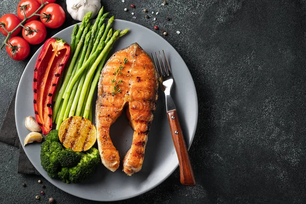 Kuşkonmaz, brokoli ve gri bir plaka üzerinde kırmızı biber ile somon steak lezzetli ve sağlıklı. Diyet yemekleri kopya alanı ile karanlık bir arka plan üzerinde. Üstten görünüm. Düz yatıyordu