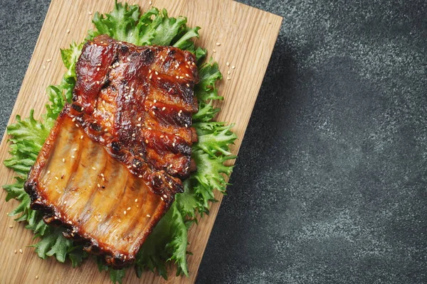 Primo piano di costolette di maiale grigliate con salsa barbecue e caramellate nel miele. Spuntino saporito a birra su una carta per limatura su sfondo concreto scuro. Vista dall'alto con spazio di copia. Posa piatta — Foto Stock