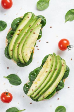 Dilimlenmiş avokado zeytin yağı, ıspanak ve keten ve susam tohumu ile iki ciabatta ekmeği. Sağlıklı vejetaryen kahvaltı beyaz arka plan üzerinde. Üstten görünüm. Düz yatıyordu