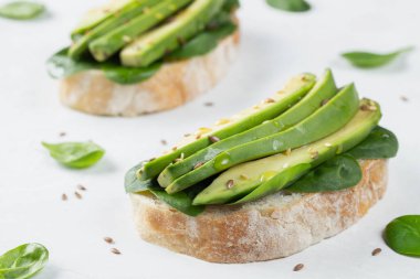 Dilimlenmiş avokado zeytin yağı, ıspanak ve keten ve susam tohumu ile iki ciabatta ekmeği. Sağlıklı vejetaryen kahvaltı beyaz arka plan üzerinde