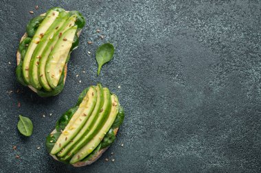 Dilimlenmiş avokado zeytin yağı, ıspanak ve keten ve susam tohumu ile iki ciabatta ekmeği. Sağlıklı vejetaryen kahvaltı kopya alanı ile karanlık bir arka plan üzerinde. Üstten görünüm. Düz yatıyordu