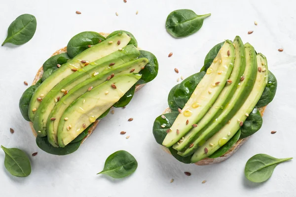 Dilimlenmiş avokado zeytin yağı, ıspanak ve keten ve susam tohumu ile iki ciabatta ekmeği. Sağlıklı vejetaryen kahvaltı beyaz arka plan üzerinde. Üstten görünüm. Düz yatıyordu.