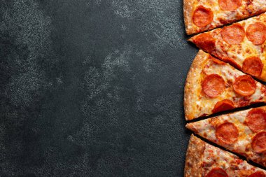 Dilimleri lezzetli taze pizza sosis sucuk ve peynir ile karanlık bir arka plan üzerinde kesmek. Üstten görünüm metin için kopya yer ile. Pizza siyah beton masada. düz lay.