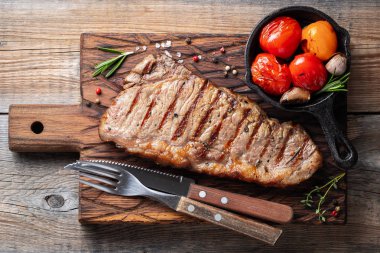 Biftek Striploin, ızgara biber, sarımsak, tuz ve kekik ile ahşap bir gemide görev yaptı. Eski ahşap rustik masa akşam yemeği için bitmiş çanak. Üstten görünüm.