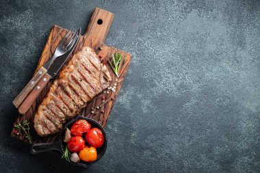 Biftek Striploin, ızgara biber, sarımsak, tuz ve kekik ile ahşap bir gemide görev yaptı. Bitmiş çanak taş karanlık bir arka plan akşam yemeği için. Kopya alanı ile üstten görünüm.