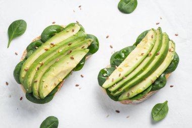 Dilimlenmiş avokado zeytin yağı, ıspanak ve keten ve susam tohumu ile iki ciabatta ekmeği. Sağlıklı vejetaryen kahvaltı beyaz arka plan üzerinde. Üstten görünüm. Düz yatıyordu.