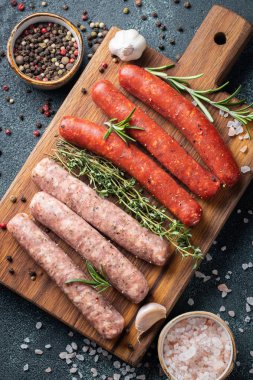 Kekik, biberiye, zeytinyağı ve sarımsak bir Ahşap Doğrama tahtası koyu bir beton tablo üzerinde çeşitli taze sosis. Siyah arka plan üzerine akşam yemeği için sosis pişirmeye hazır. Kopya alanı ile üstten görünüm.