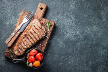 Biftek Striploin, ızgara biber, sarımsak, tuz ve kekik ile ahşap bir gemide görev yaptı. Bitmiş çanak taş karanlık bir arka plan akşam yemeği için. Kopya alanı ile üstten görünüm.