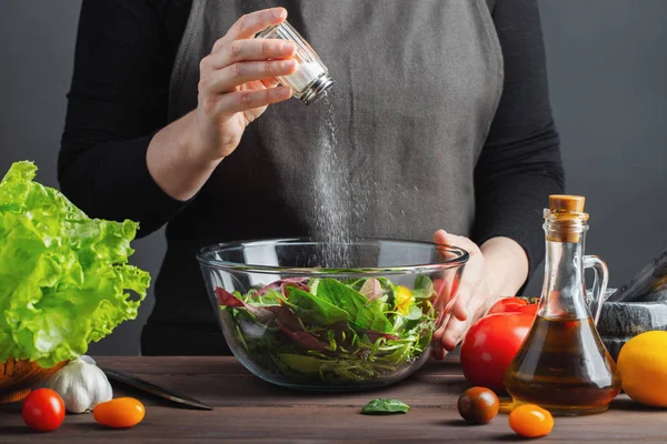 Woman chef in the kitchen preparing vegetable salad. Healthy Eating. Diet Concept. A Healthy Way Of Life. To Cook At Home. For Cooking. The girl sprinkles salt in a salad on a dark background.