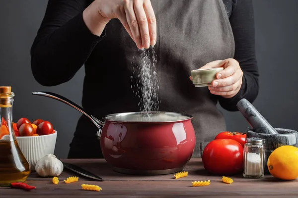 Şef hazırlıklar spagetti ve makarna, karanlık bir arka plan yemek kavramının tuzlu su. Su makarna düdük pişirmeden önce tuzlama kadın.