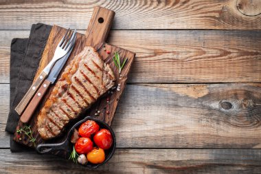 Biftek Striploin, ızgara biber, sarımsak, tuz ve kekik ile ahşap bir gemide görev yaptı. Eski ahşap rustik masa akşam yemeği için bitmiş çanak. Kopya alanı ile üstten görünüm.