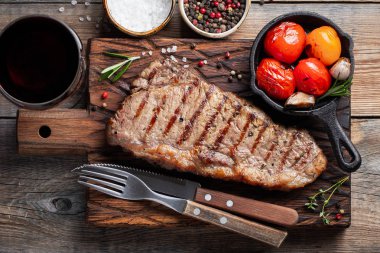 Biftek Striploin, ızgara biber, sarımsak, tuz ve kekik ile ahşap bir gemide görev yaptı. Bitmiş yemek eski ahşap rustik masa üzerinde kırmızı şarap ile akşam yemeği için. Üstten görünüm.