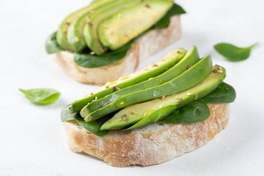 Dilimlenmiş avokado zeytin yağı, ıspanak ve keten ve susam tohumu ile iki ciabatta ekmeği. Sağlıklı vejetaryen kahvaltı beyaz arka plan üzerinde