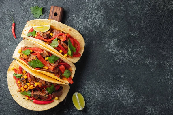 Meksykańskie tacos z wołowiną, warzywami i salsy. Tacos al pastor na desce na czarnym tle. Widok z góry z miejsca kopii — Zdjęcie stockowe