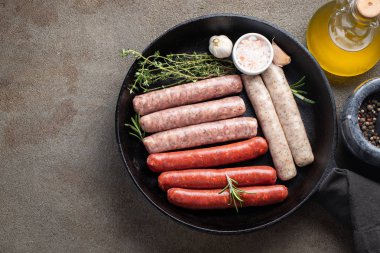 Kekik, biberiye ve dökme demir sarımsak ile çeşitli taze çiğ sosis karanlık bir beton masaya pan. Üstten görünüm kopya alanı ile. Düz yatıyordu.