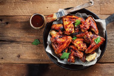Fırında tavuk kanadı bir döküm Barbekü sosu içinde eski bir ahşap rustik masa üzerinde pan. Kopya alanı ile üstten görünüm.