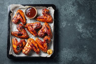 Barbekü soslu susam ve karanlık bir tablo üzerinde bir fırın tepsisinde maydanoz ile kavrulmuş tavuk kanatları. Üstten görünüm kopya alanı ile. Lezzetli Aperatif karanlık bir arka plan üzerinde bira için. Düz yatıyordu.