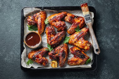 Barbekü soslu susam ve karanlık bir tablo üzerinde bir fırın tepsisinde maydanoz ile kavrulmuş tavuk kanatları. Üstten görünüm. Lezzetli Aperatif karanlık bir arka plan üzerinde bira için. Düz yatıyordu.