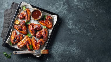 Barbekü soslu susam ve karanlık bir tablo üzerinde bir fırın tepsisinde maydanoz ile kavrulmuş tavuk kanatları. Üstten görünüm kopya alanı ile. Lezzetli Aperatif karanlık bir arka plan üzerinde bira için. Düz yatıyordu.