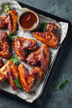 Barbekü soslu susam ve karanlık bir tablo üzerinde bir fırın tepsisinde maydanoz ile kavrulmuş tavuk kanatları. Üstten görünüm. Lezzetli Aperatif karanlık bir arka plan üzerinde bira için. Düz yatıyordu.