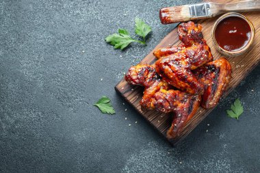 Barbekü soslu susam ve beton bir masada ahşap bir gemide maydanoz ile kavrulmuş tavuk kanatları. Üstten görünüm kopya alanı ile. Lezzetli Aperatif karanlık bir arka plan üzerinde bira için. Düz yatıyordu.