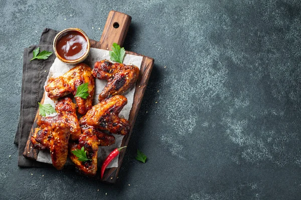 Barbekü soslu susam ve beton bir masada ahşap bir gemide maydanoz ile kavrulmuş tavuk kanatları. Üstten görünüm kopya alanı ile. Lezzetli Aperatif karanlık bir arka plan üzerinde bira için. Düz yatıyordu.