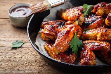 Fırında tavuk kanadı bir döküm Barbekü sosu içinde eski bir ahşap rustik masa üzerinde tava.