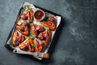 Barbekü soslu susam ve karanlık bir tablo üzerinde bir fırın tepsisinde maydanoz ile kavrulmuş tavuk kanatları. Üstten görünüm kopya alanı ile. Lezzetli Aperatif karanlık bir arka plan üzerinde bira için. Düz yatıyordu.