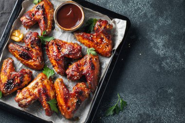 Barbekü soslu susam ve karanlık bir tablo üzerinde bir fırın tepsisinde maydanoz ile kavrulmuş tavuk kanatları. Üstten görünüm kopya alanı ile. Lezzetli Aperatif karanlık bir arka plan üzerinde bira için. Düz yatıyordu.