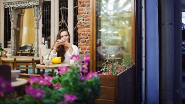 Akşam bir bardak çay ile parlak ve sıcak kafede oturan ve pencereden dışarı bakıp genç çekici kız. Karanlık ve soğuk sokaktır. Konfor kavramını.