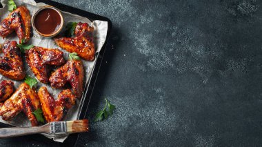 Barbekü soslu susam ve karanlık bir tablo üzerinde bir fırın tepsisinde maydanoz ile kavrulmuş tavuk kanatları. Üstten görünüm kopya alanı ile. Lezzetli Aperatif karanlık bir arka plan üzerinde bira için. Düz yatıyordu.