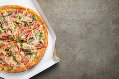 İtalyan lokanta. Lezzetli sıcak pizza jambon ve dilimlenmiş ve kahverengi beton masaya servis petrol bir kutu içinde görünümü kapatın. Menü fotoğraf. Üstten Görünüm kopya alanı ile. Düz yatıyordu
