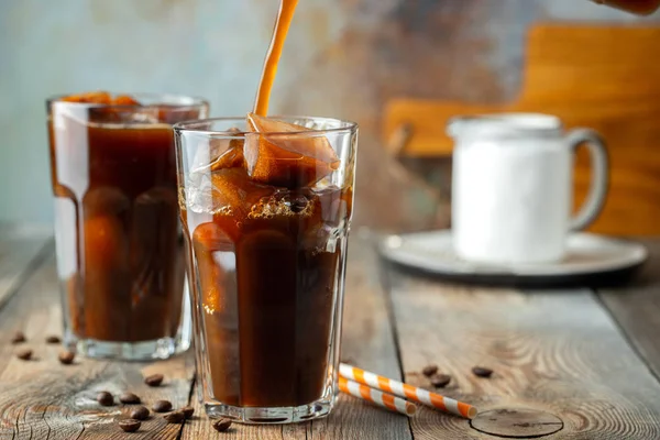 Uzun bir bardak kahve üzerine döktü krem, kahve buz küpleri ile eski rustik ahşap masa fasulyeli buz. Soğuk yaz içeceği tüpler üzerinde mavi bir paslı arka plan kopya alanı ile.