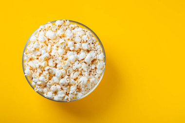 Sarı arka planda tuzlanmış patlamış mısırlı cam kase. Kopyalama alanı olan üst görünüm. Düz yatıyordu.