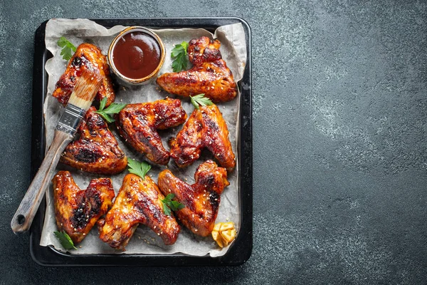 Pečená kuřecí křídla v barbecue omáčce s Sezamová semínka a petržel v pekáč na tmavý stůl. Pohled shora s kopie prostoru. Chutný snack pro pivo na tmavém pozadí. Rozložení bytu — Stock fotografie