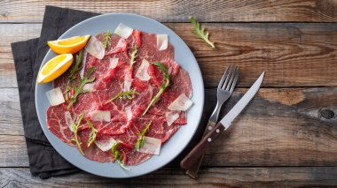 Ahşap masa üzerinde arugula, limon ve parmesan peyniri ile Mermer sığır carpaccio. . Üst görünüm, kopyalama alanı ile düz yatıyordu