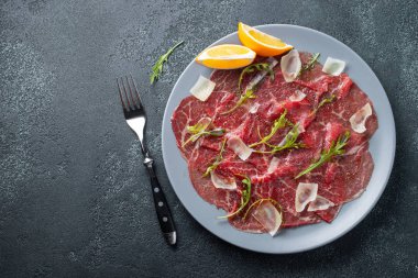 Koyu beton masa üzerinde arugula, limon ve parmesan peyniri ile Mermer sığır carpaccio. Üst görünüm, kopyalama alanı ile düz yatıyordu