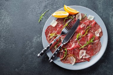 Koyu beton masa üzerinde arugula, limon ve parmesan peyniri ile Mermer sığır carpaccio. Üst görünüm, kopyalama alanı ile düz yatıyordu