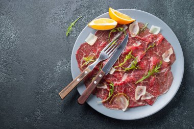 Koyu beton masa üzerinde arugula, limon ve parmesan peyniri ile Mermer sığır carpaccio. Üst görünüm, kopyalama alanı ile düz yatıyordu