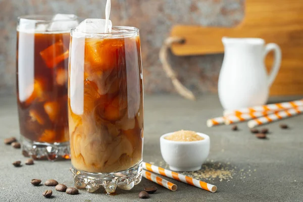 Es kopi dalam gelas tinggi dengan krim dituangkan di atas dan biji kopi. Minuman musim panas yang dingin di latar belakang coklat berkarat — Stok Foto