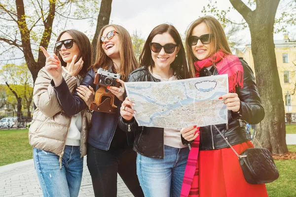 Un gruppo di giovani donne turistiche è alla ricerca di attrazioni in una città europea sulla mappa. Quattro donne allegre e belle passeggiano per la città primaverile in occhiali da sole . — Foto Stock