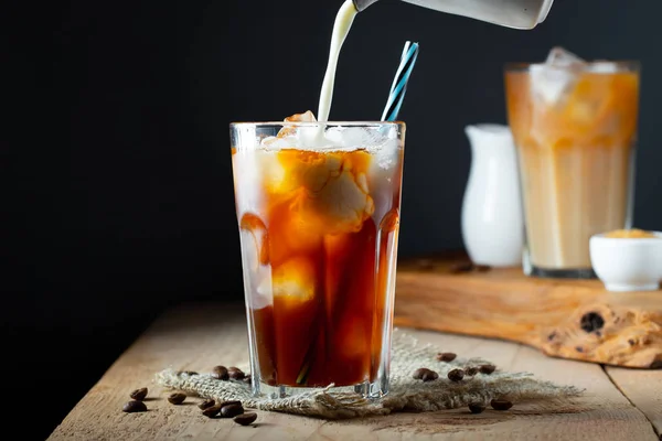 Es kopi dalam gelas tinggi dengan krim dituangkan di atas, es batu dan kacang-kacangan di atas meja kayu pedesaan tua. Minuman musim panas yang dingin dengan tabung di latar belakang hitam dengan ruang fotokopi — Stok Foto