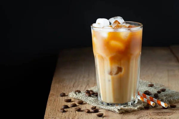 Eiskaffee in einem hohen Glas mit Sahne, Eiswürfeln und Bohnen auf einem alten rustikalen Holztisch. kaltes Sommergetränk mit Röhren auf schwarzem Hintergrund mit Kopierraum — Stockfoto