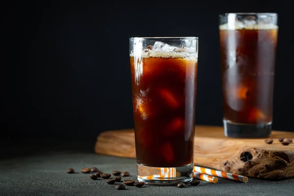 Ijskoffie in een hoog glas met room gegoten over, ijsblokjes en bonen op een oude rustieke houten tafel. Koude zomer drank met tubes op een zwarte achtergrond met Kopieer ruimte — Stockfoto