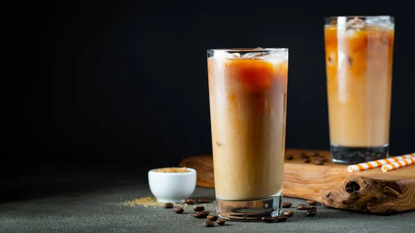 Es kopi dalam gelas tinggi dengan krim dituangkan di atas, es batu dan kacang-kacangan di atas meja kayu pedesaan tua. Minuman musim panas yang dingin dengan tabung di latar belakang hitam dengan ruang fotokopi — Stok Foto